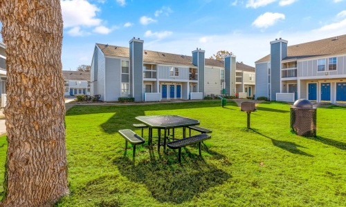 a table and chairs in a grassy area with buildings in the background