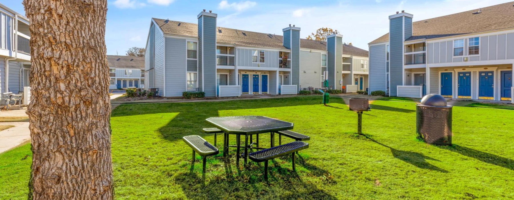 a table and chairs in a grassy area with buildings in the background